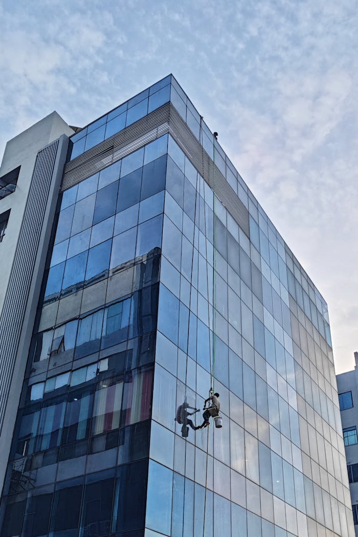 Window cleaners working on a tall glass building in an urban setting during the daytime.