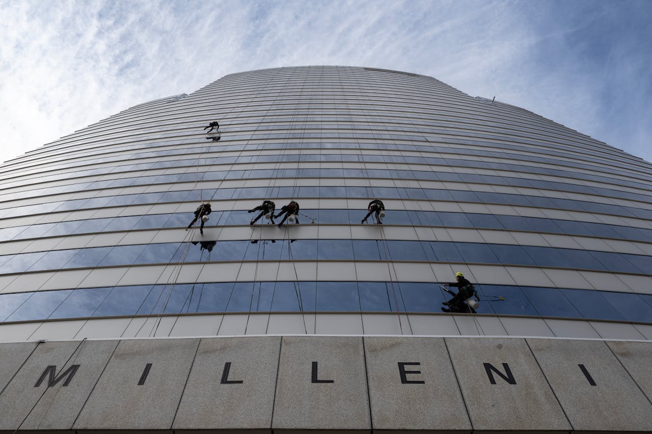 Window cleaners suspended high up a Santiago skyscraper against a vibrant sky.